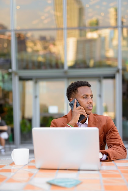 Retrato del empresario africano al aire libre en la cafetería con ordenador portátil