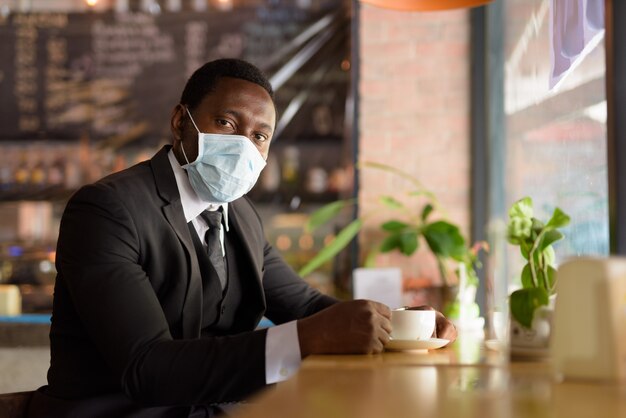 Retrato del empresario africano con máscara dentro de la cafetería como la nueva normalidad