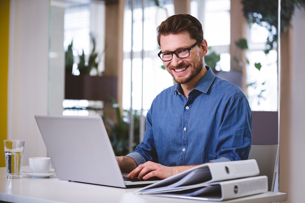 Retrato del empresario alegre que trabaja en la computadora portátil en la oficina creativa