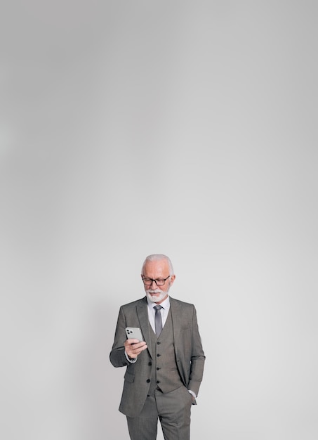 Retrato de un empresario de alto rango con la mano en el bolsillo enviando mensajes a través de un teléfono inteligente sobre un fondo blanco