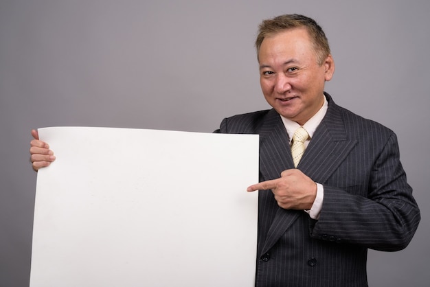 Retrato del empresario asiático maduro contra la pared gris