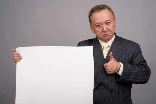 Retrato del empresario asiático maduro contra la pared gris