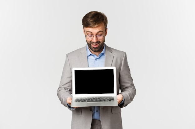 Retrato de empresario barbudo y gafas, mostrando y mirando la pantalla del portátil