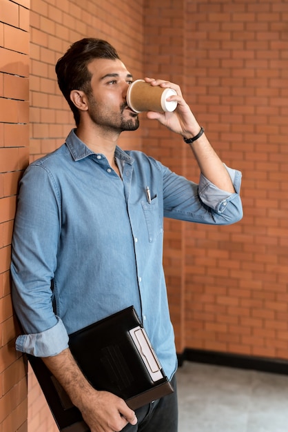 Retrato del empresario caucásico de Oriente Medio tomando café de la taza de café desechable para llevar y el portapapeles en la sala de reuniones después del almuerzo.