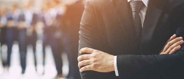 Retrato de un empresario CEO de pie con el brazo cruzado de la mano exitoso equipo de negocios en un clásico traje negro con un empleado en segundo plano.