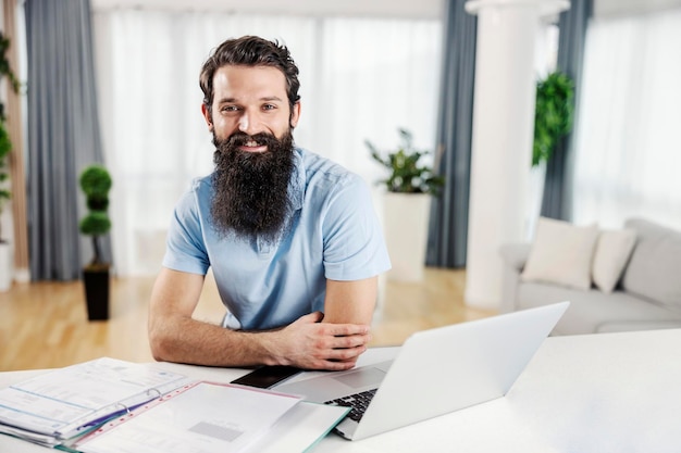 Retrato de un empresario feliz sentado en su acogedora casa y trabajando mientras mira la cámara