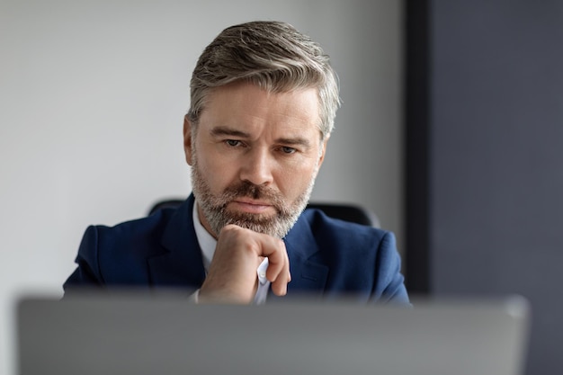 Retrato de un empresario de mediana edad enfocado mirando la pantalla de un portátil en la oficina