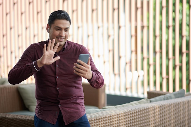 Retrato de empresario positivo saludando con la mano cuando llama por video a su compañero de trabajo