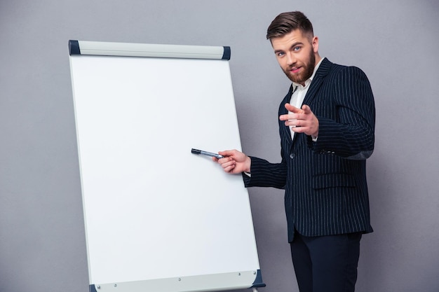 Retrato de un empresario seguro que presenta algo en tablero en blanco sobre pared gris