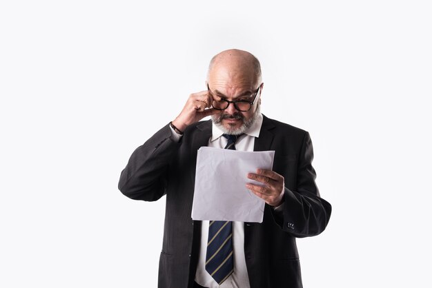 Retrato del empresario senior asiático indio sosteniendo o leyendo documentos en papel mientras está de pie contra el fondo blanco.