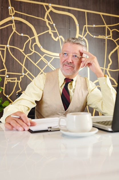 Retrato de empresario senior pensativo sentado en la mesa de café y trabajando en el plan de negocios