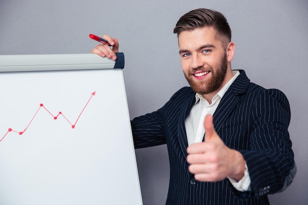 Retrato de un empresario sonriente dando pulgares mientras dibuja el gráfico