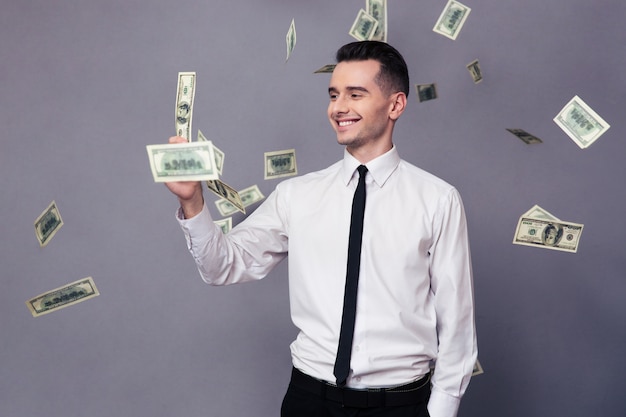 Retrato de un empresario sonriente de pie bajo la lluvia con dinero sobre pared gris