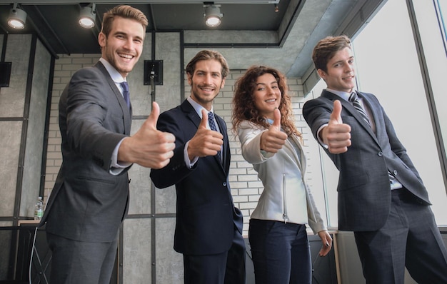 Retrato de empresarios felices de pie en la oficina mostrando el pulgar hacia arriba