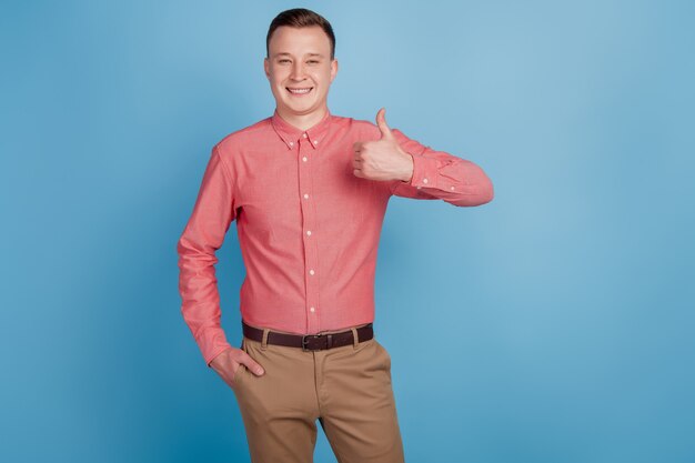 Retrato de encantador chico agradable positivo levantar el pulgar hacia arriba sobre fondo azul.