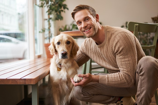 Retrato de un encantador golden retriever y un hombre guapo en una cafetería un lindo perro da una pata y toma una foto