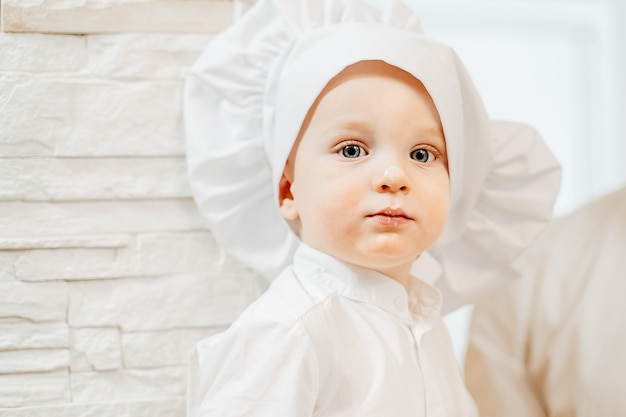 Retrato de un encantador niño de dos años de ojos azules manchados de harina mientras cocina pasteles caseros