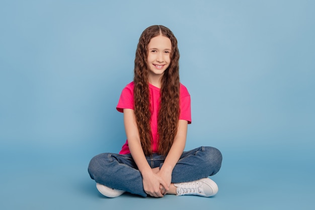 Retrato de encantador sueño positivo niña sentarse piso sujetar las piernas sobre fondo azul.