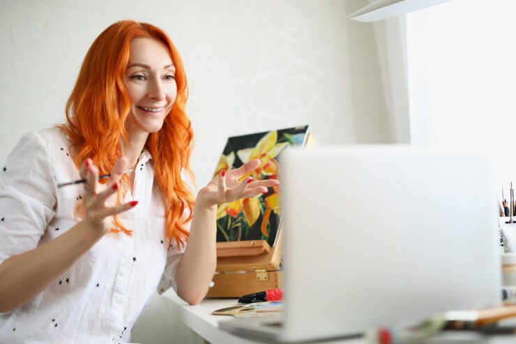 Foto retrato de una encantadora artista femenina gesticulando y hablando en una laptop alegre pintor sosteniendo