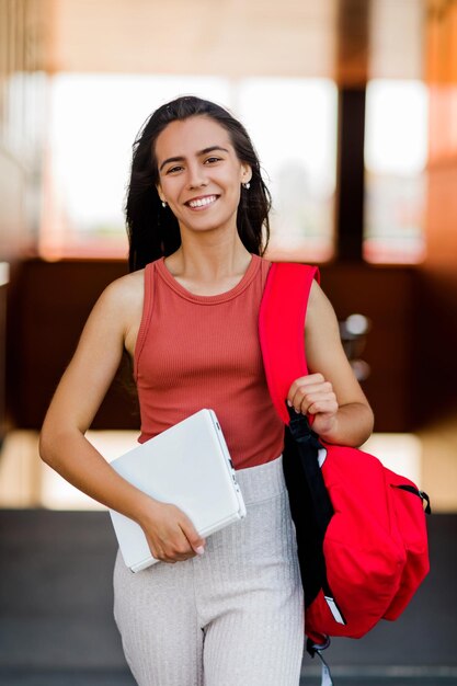 Foto retrato de una encantadora estudiante con una mochila y una computadora portátil