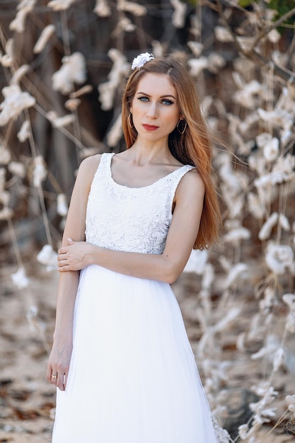 Retrato de una encantadora joven rubia con un vestido blanco ligero y aireado posando sobre un fondo de corales blancos. Concepto de ternura.