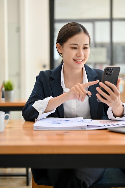 Retrato Encantadora mujer de negocios asiática usando su teléfono inteligente para chatear con su colega