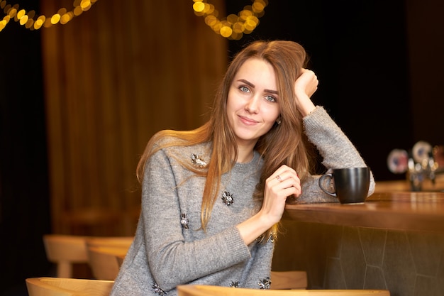 Retrato encantadora mulher atraente, com cabelos longos e sorriso amigável localização no café e tomando café.