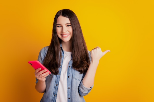 Retrato de encantadora niña alegre sosteniendo en las manos el espacio vacío del lado del pulgar directo del teléfono