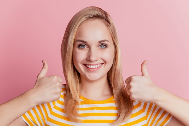 Retrato de encantadora niña positiva aprobar gesto pulgar hacia arriba sonrisa con dientes sobre fondo rosa