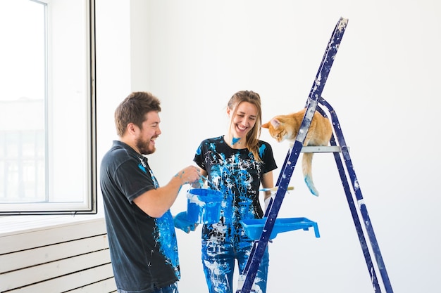 Retrato de encantadora pareja divertida con gato haciendo redecoración en apartamento.