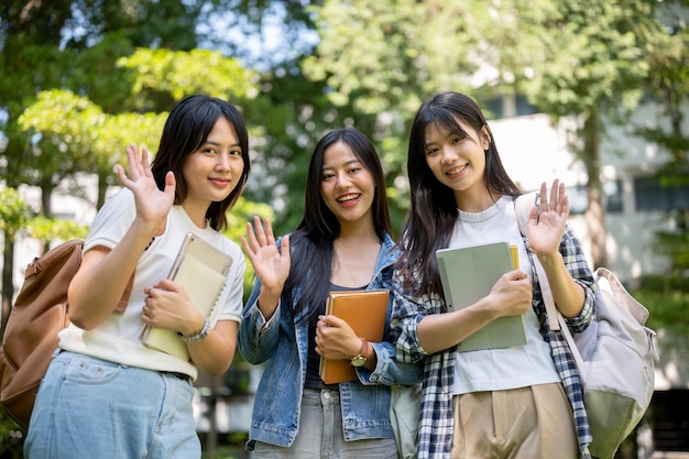 Retrato de encantadoras y amigables estudiantes universitarias asiáticas saludando y sonriendo a la cámara