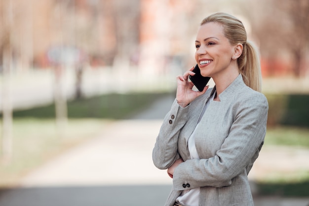 Retrato de un encargado de sexo femenino positivo que habla en un teléfono al aire libre, espacio de la copia.