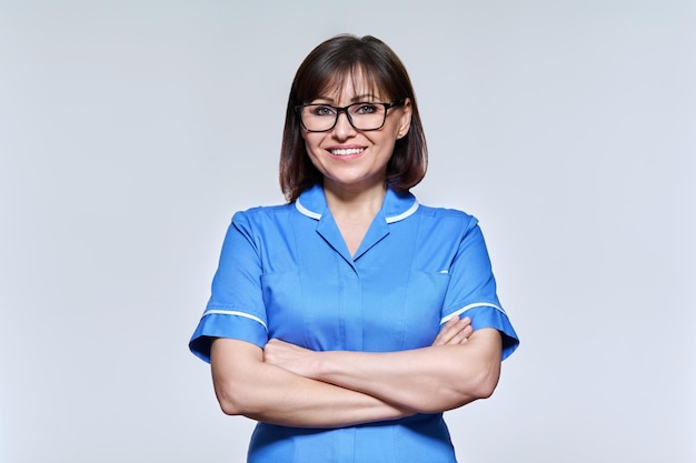 Retrato de una enfermera de mediana edad con uniforme azul mirando a la cámara en un estudio claro