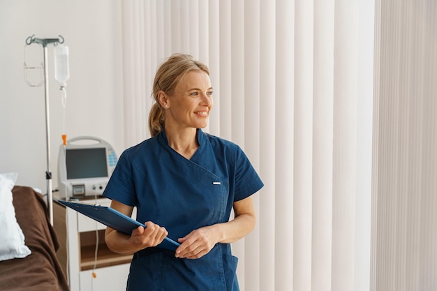 Retrato de una enfermera sonriente sosteniendo una tableta mientras está en la sala del hospital y mirando hacia otro lado