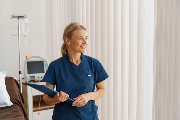 Foto retrato de una enfermera sonriente sosteniendo una tableta mientras está en la sala del hospital y mirando hacia otro lado