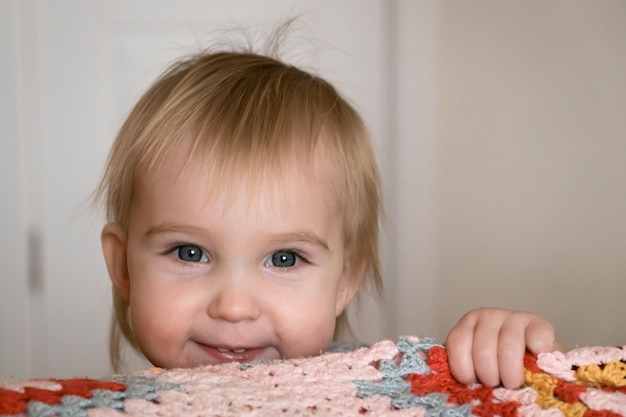 Retrato engraçado da cara engraçada da menina loura da criança sorridente feliz em casa