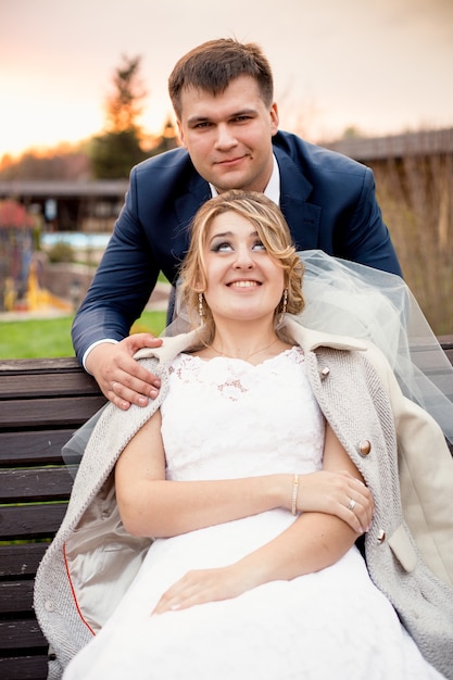 Retrato engraçado de lindo noivo abraçando a linda noiva sentada no banco