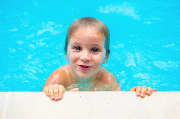 Retrato engraçado foto feliz sorriso humor estilo de vida Criança travessa menino sardento cabeça molhada ombros mãos brincar nadar na piscina água Expressão do rosto gesto olhar para a câmera Comportamento esportivo da infância