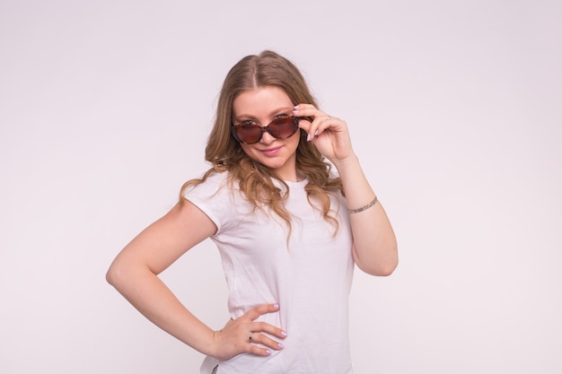 Retrato de enigmática hermosa chica blanca arreglando el cabello con gafas de sol en blanco.