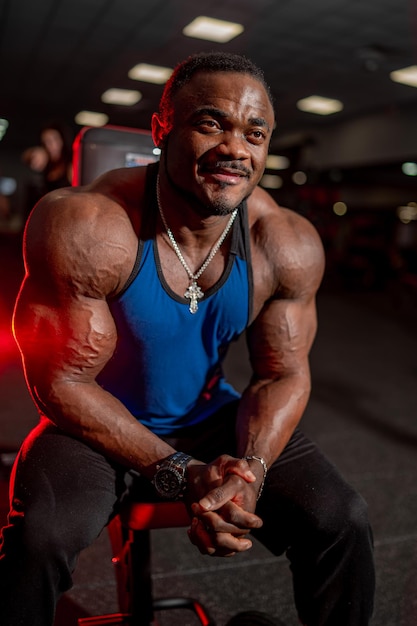 Retrato de un entrenador de fitness masculino afroamericano Bodybuilder muestra bíceps y mira el fondo del gimnasio lateral