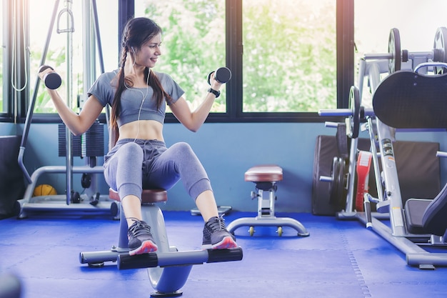 Retrato del entrenamiento muscular del culturista de la mujer del ajuste con pesas de gimnasia en gimnasio de la aptitud.