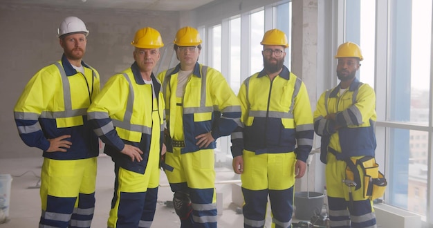Retrato de equipo multiétnico de constructores en uniforme posando en la cámara en el sitio de construcción