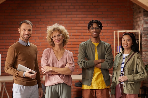 Retrato de equipo de negocios creativos multiétnicos de pie con los brazos cruzados y sonriendo a la cámara en la oficina