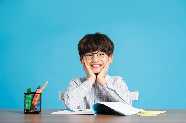 Retrato de un escolar sentado y estudiando en un fondo azul.