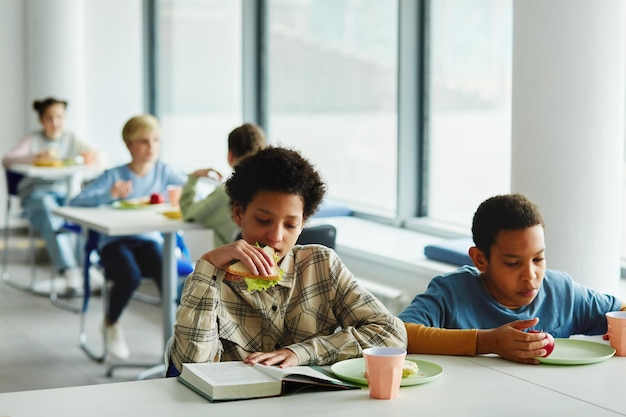 Retrato de escolares en el almuerzo se centran en la joven afroamericana comiendo sándwich y r