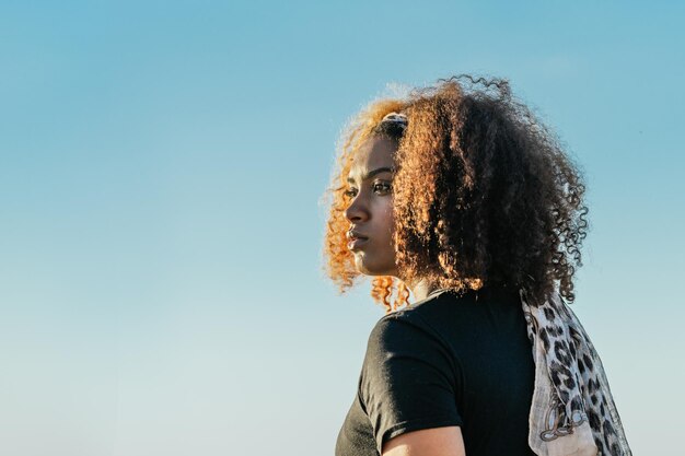 Retrato con espacio de copia de una mujer latina con cabello rizado mirando el horizonte en un día soleado