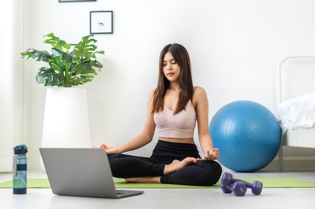 Retrato esporte beleza asiática corpo mulher magra em roupas esportivas sentada relaxe e garota praticando ioga e faça exercícios de fitness com computador portátil no quarto em casaconceito de dietafitness e saudável