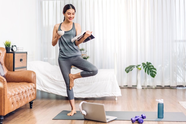 Retrato esporte beleza asiática corpo mulher magra em roupas esportivas sentada relaxe e garota praticando ioga e faça exercícios de fitness com computador portátil no quarto em casaconceito de dietafitness e saudável