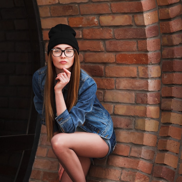Retrato de estilo de vida al aire libre de una chica joven y bonita, vestida con estilo grunge botín hipster sobre fondo urbano