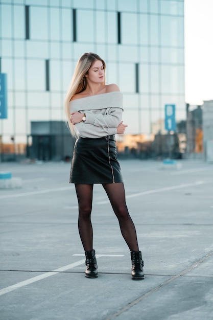 Retrato de estilo de vida al aire libre de una impresionante chica rubia caminando por la calle de la ciudad vistiendo